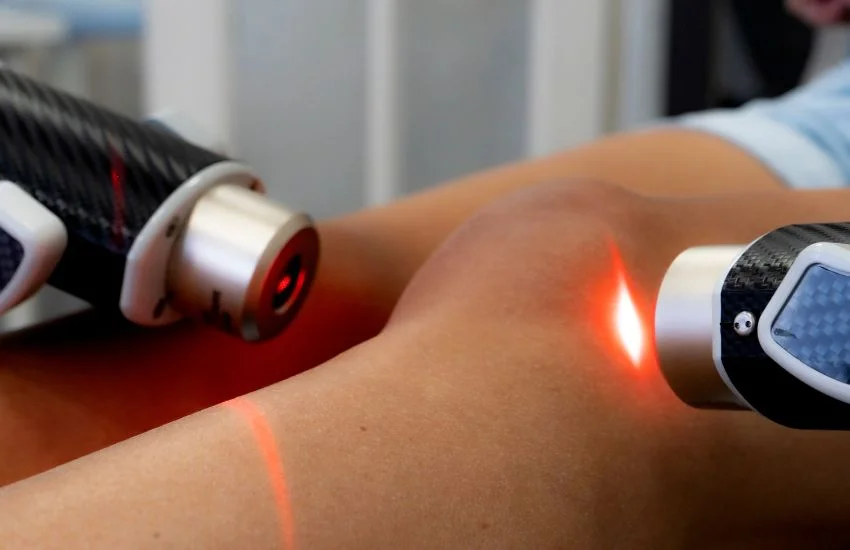 Dispositivo de terapia láser aplicado sobre la rodilla de un paciente para tratar la tendinitis rotuliana, con luz roja enfocada en la zona inflamada.